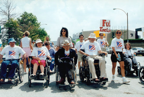Protesters ride with Justin Dart Jr. and Max Starkloff in a St. Louis march through the streets. Many of the protesters use wheelchairs.